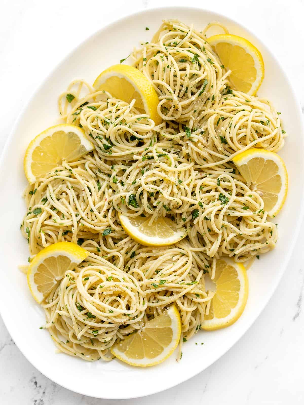 Overhead view of an oval platter full of lemon parsley pasta with lemon slices as garnish