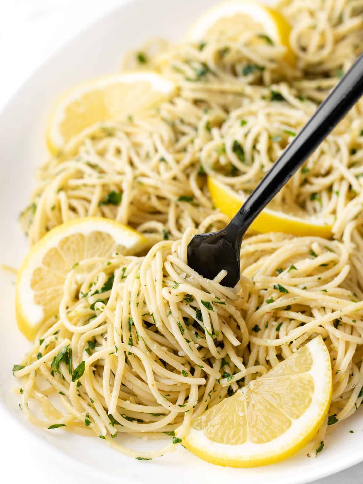 Close up of a fork twirling some of the lemon parsley pasta on a platter with sliced lemons as garnish