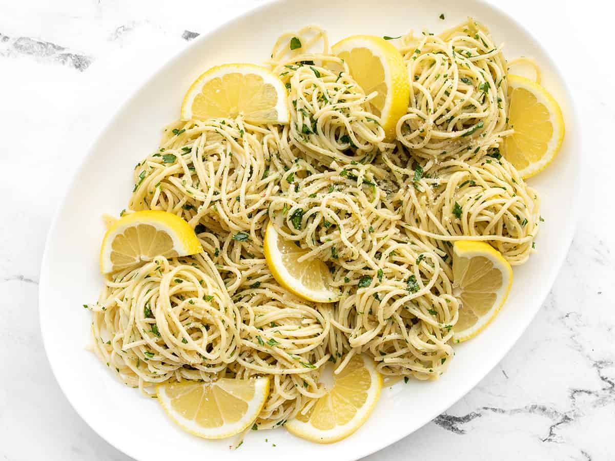 Overhead view of lemon parsley pasta on an oval serving dish with lemon slices as garnishes