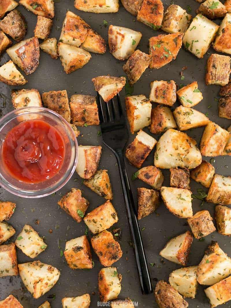 Parmesan Roasted Potatoes on a baking sheet with a dish of ketchup and a black fork