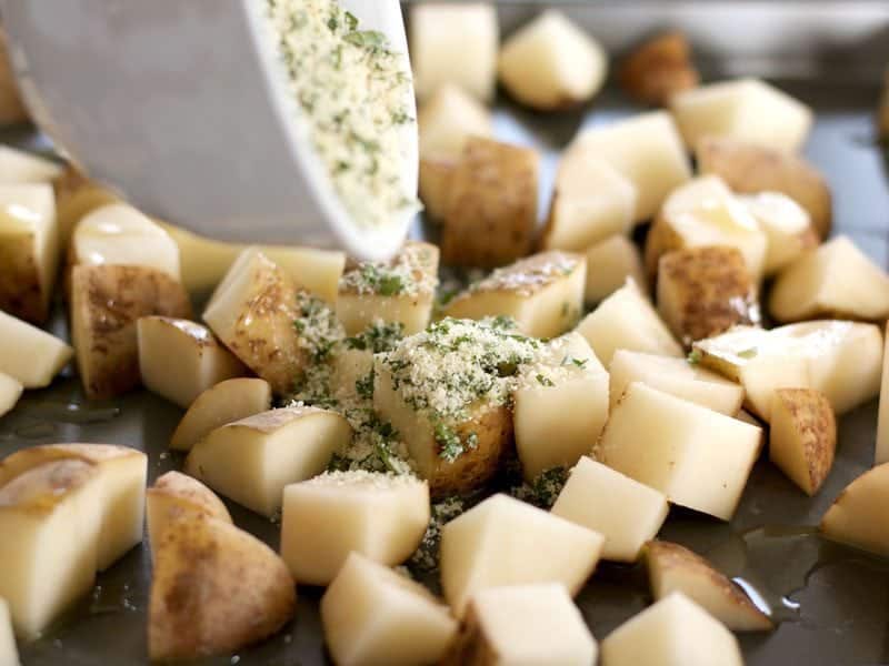 Parmesan seasoning being poured over cubed potatoes