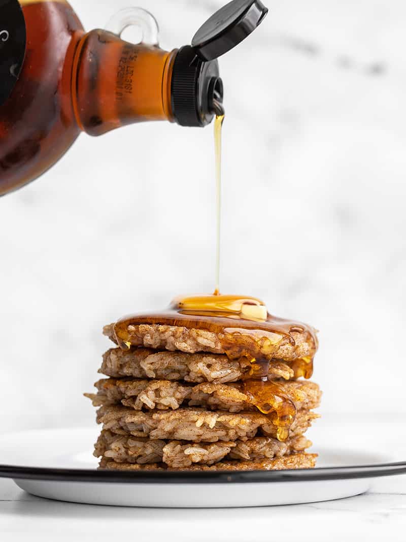 Side view of a stack of rice pancakes with butter and syrup being poured over top