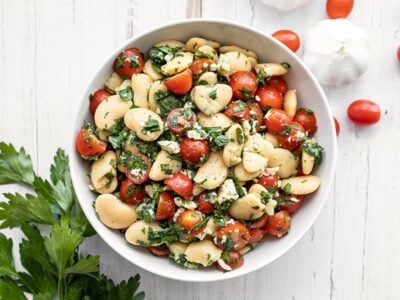 Overhead view of a bowl full of Mediterranean White Bean Salad with parsley, tomatoes, and garlic on the side