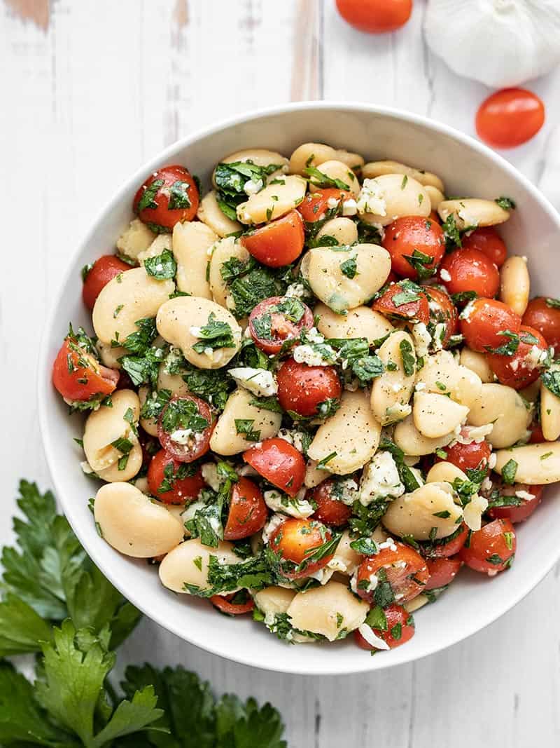 A big bowl full of Mediterranean White Bean Salad with tomatoes and parsley on the side