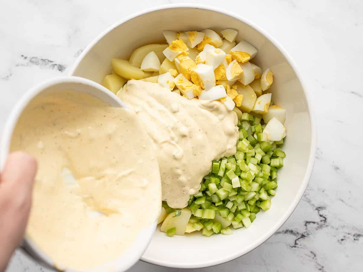 Dressing being poured into the bowl with the potato salad ingredients