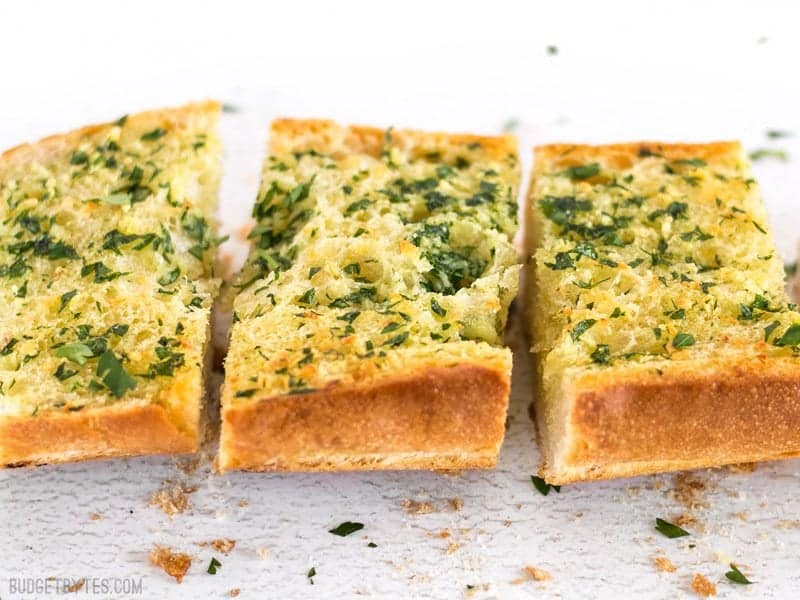 Side view of a baked loaf of homemade garlic bread, sliced into sections and garnished with fresh parsley