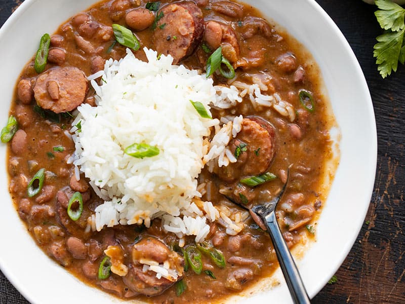 Close up overhead view of a bowl full of red beans topped with a scoop of rice, parsley, and green onion.