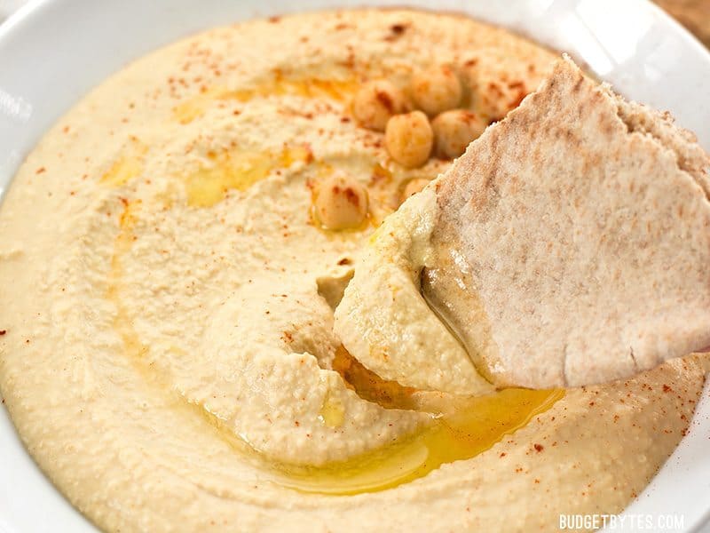Close up of pita bread being dipped into Homemade Hummus