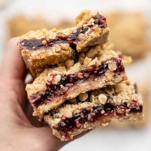 A hand holding a stack of raspberry oatmeal bars close to the camera