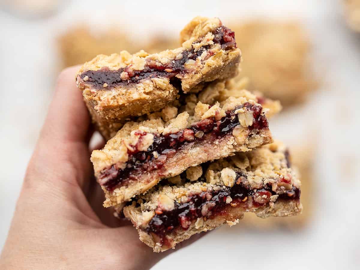 A hand holds a stack of raspberry oatmeal bars close to the camera