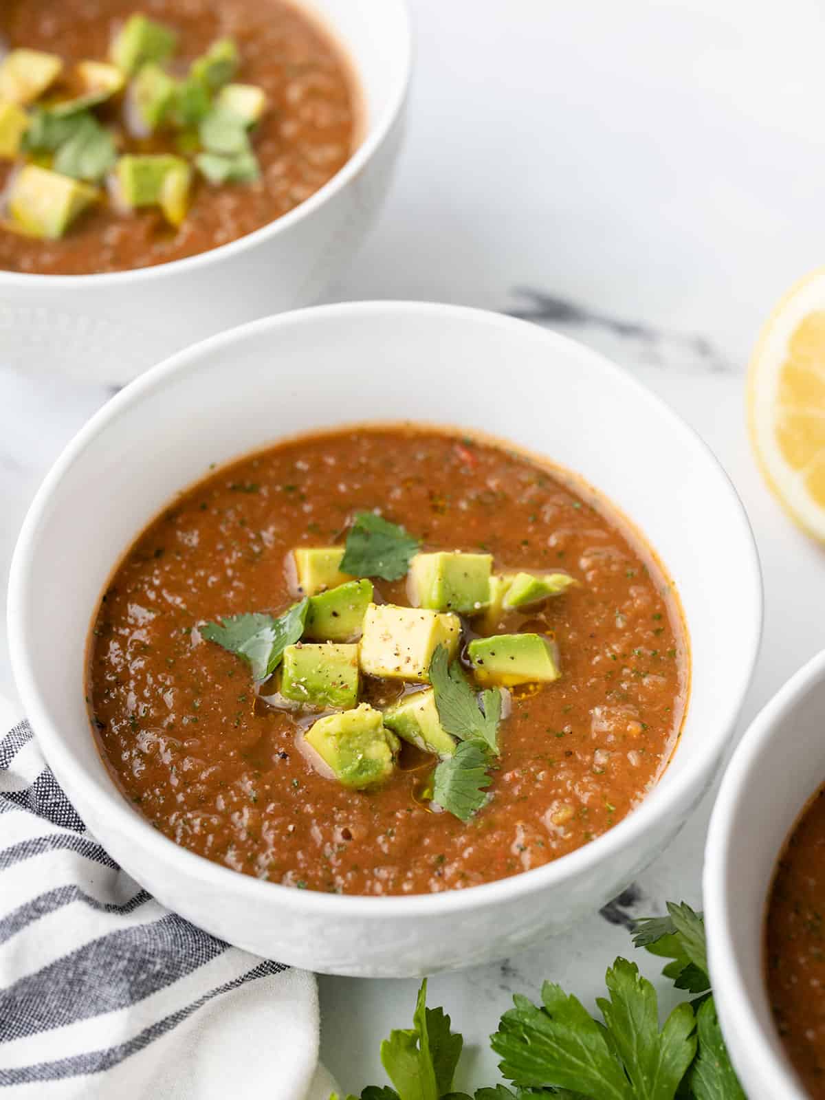 side view of three bowls of summer gazpacho topped with avocado