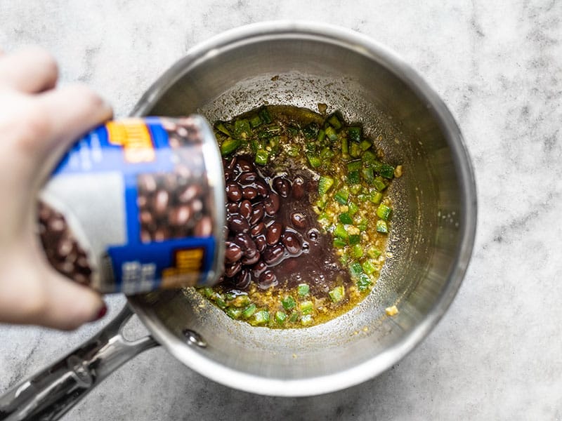 A can of black beans being poured into the sauce pot.