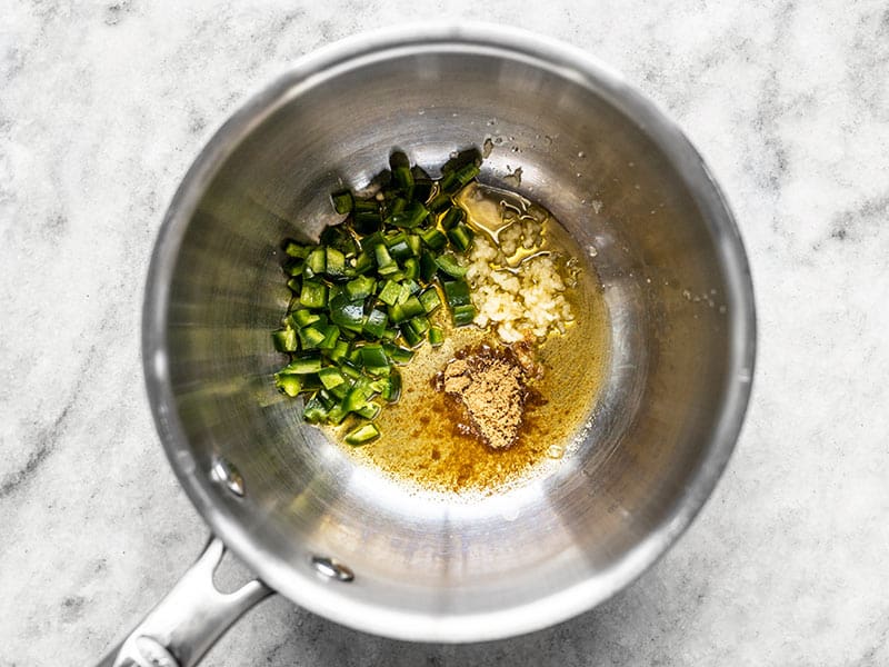 Diced jalapeño, minced garlic, cumin, and oil in a sauce pot.