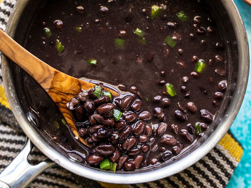 Close up of quick seasoned black beans in the sauce pot, being lifted by a wooden spoon.