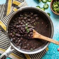 A pot of quick seasoned black beans, with a wooden spoon, jalapeños and green onion on the side