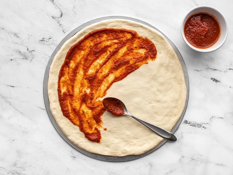 Pizza sauce being spread on stretched dough