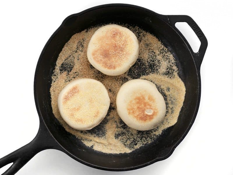 Cooked English Muffins in a cast iron skillet with a lot of cornmeal