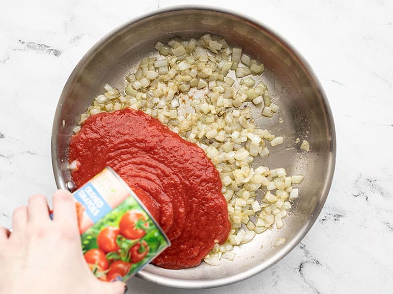 Crushed tomatoes pouring into skillet