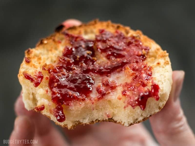 Close up of a hand holding a Homemade English muffin smeared with raspberry jam.