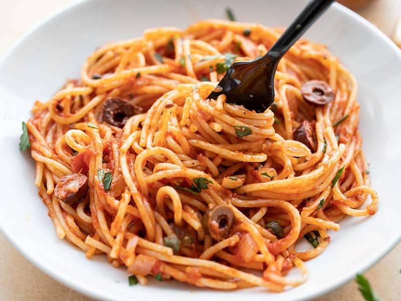 Pasta puttanesca is an original budget-friendly meal with inexpensive pasta that gets a flavor kick from ingredients like anchovies, olives, and garlic. BudgetBytes.com Front view of a bowl of Pasta Puttanesca with a fork twirling the pasta.