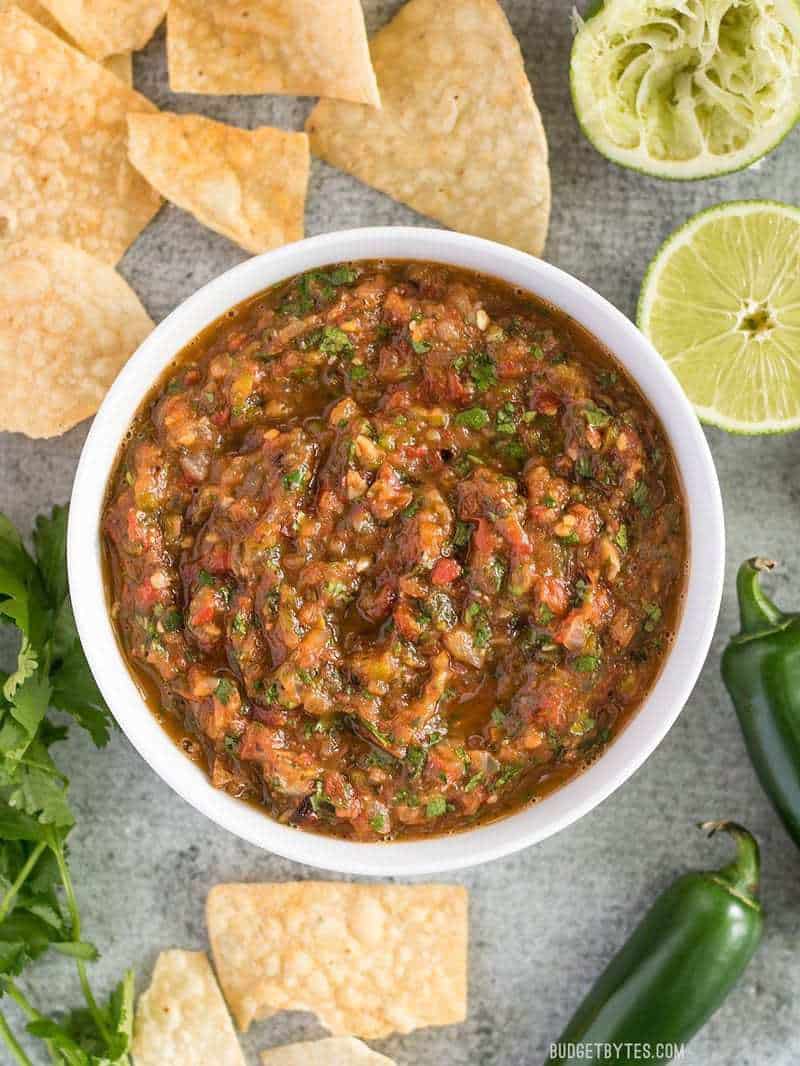 Fire Roasted Salsa in white bowl with tortilla chips, limes and jalapeño on side