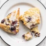 Two lemon blueberry scones on a plate, one partially crumbled