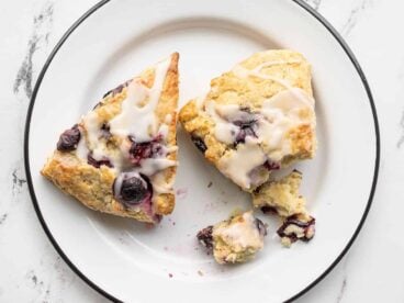 Two lemon blueberry scones on a plate, one partially crumbled