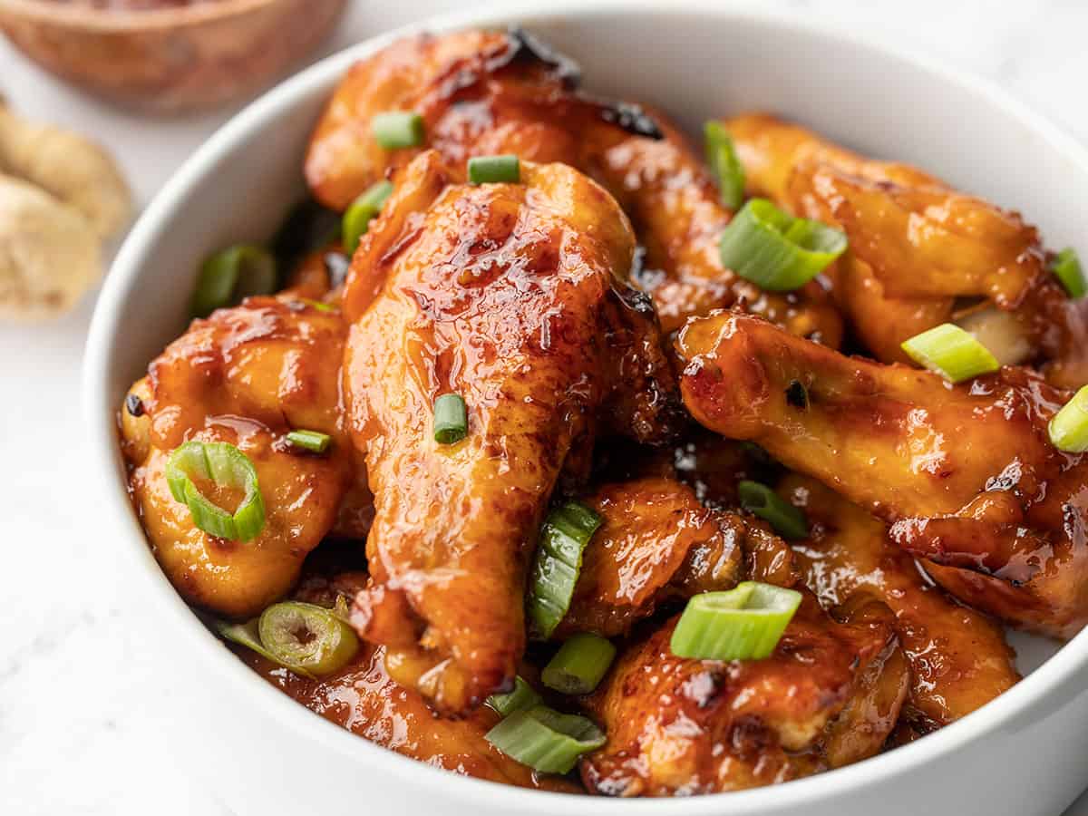 Close up side view of a bowl full of sticky ginger chicken wings