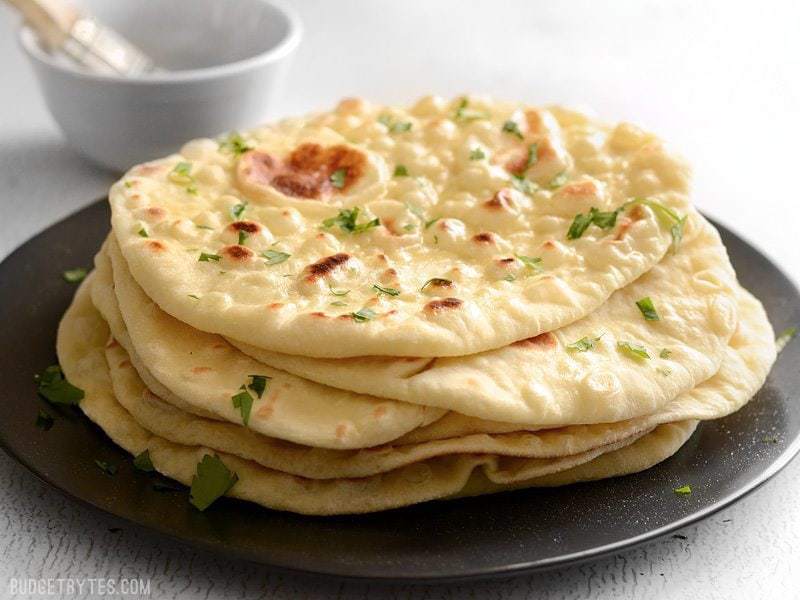 A stack of warm, pillowy homemade naan bread, brushed with butter.