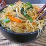 Singapore Noodles Singapore Noodles, Rice Vermicelli in black bowl with chop sticks and a bottle of Sriracha on the side