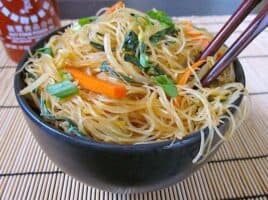 Singapore Noodles Singapore Noodles, Rice Vermicelli in black bowl with chop sticks and a bottle of Sriracha on the side