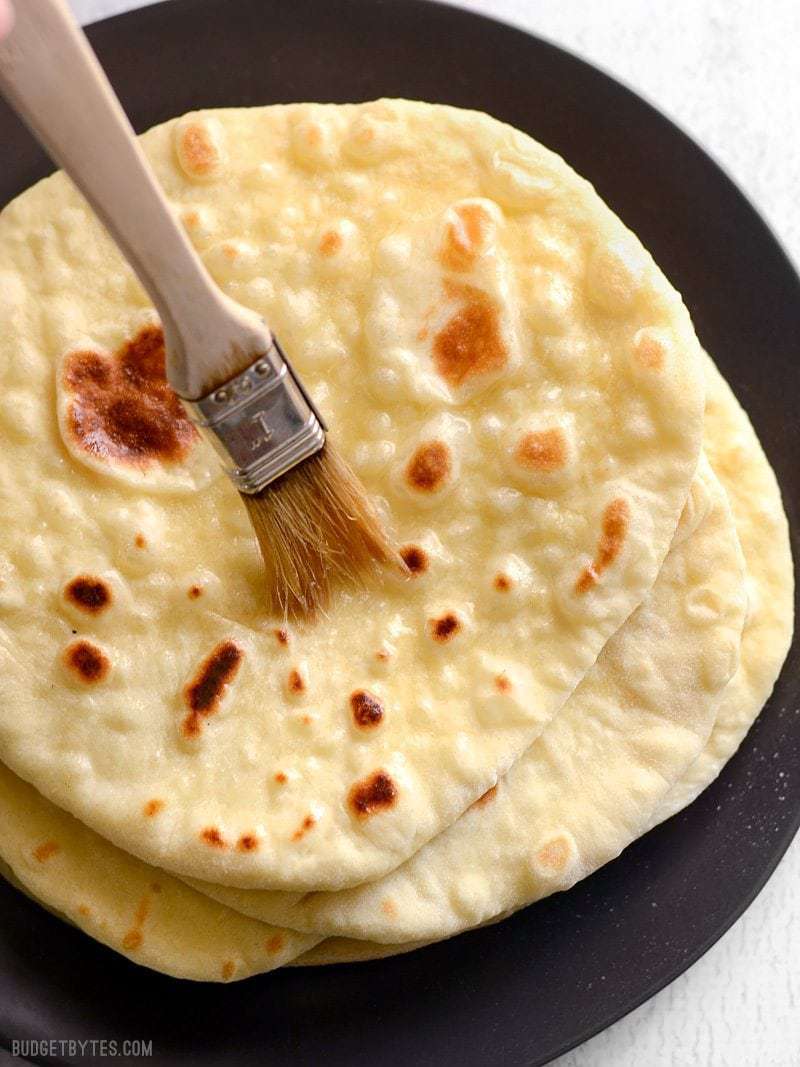 Homemade naan bread being brushed with melted butter.