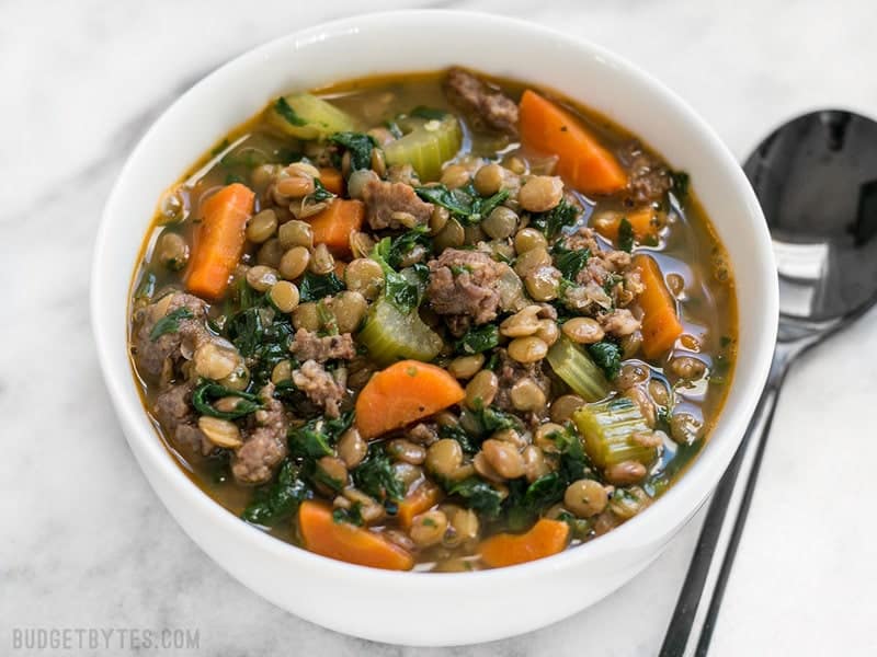 Lentil & Sausage Stew in white bowl with spoon on the side