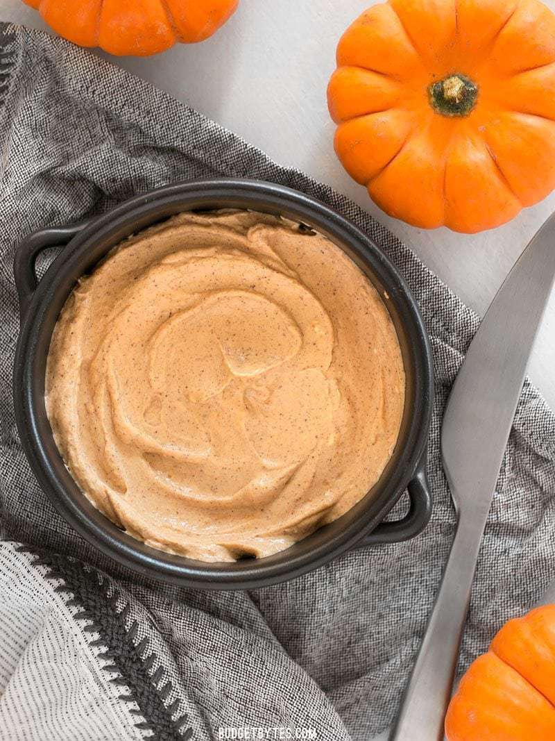 Pumpkin cream cheese spread in pan on top of grey napkin with knife and mini pumpkins on side