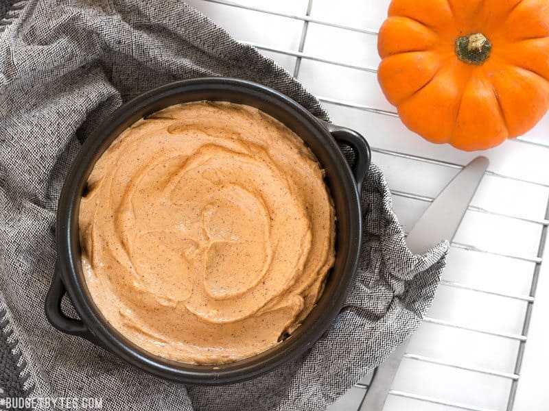 Pumpkin cream cheese spread in pan on grey napkin with knife and mini pumpkin on side 