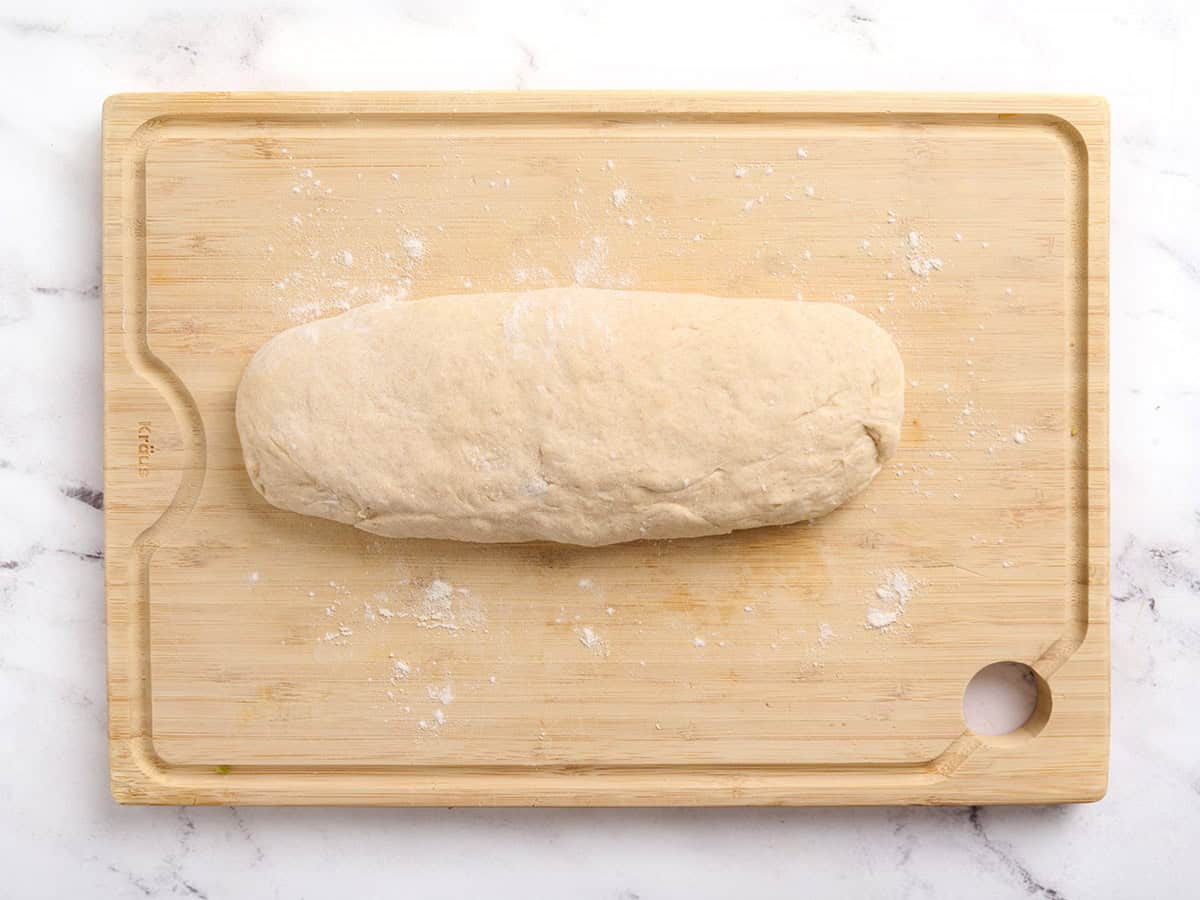 Pita bread dough formed into a log on a wooden cutting board.