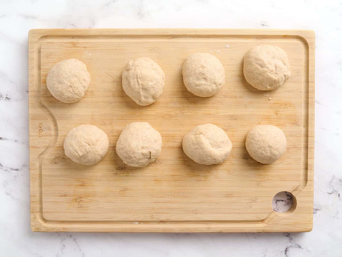 Eight dough balls on a wooden cutting board.