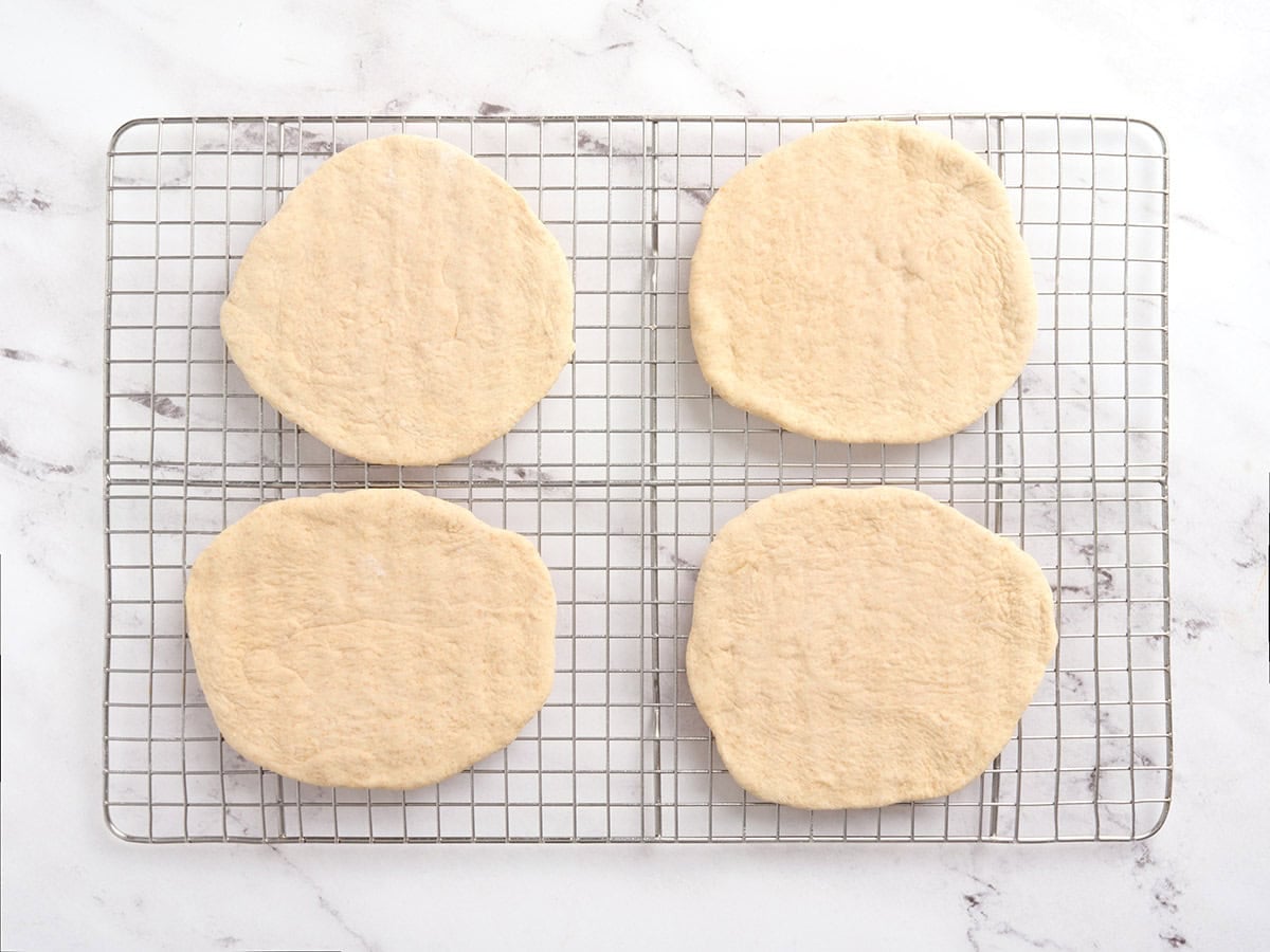 Four portions of dough rolled into circles on a wire rack.