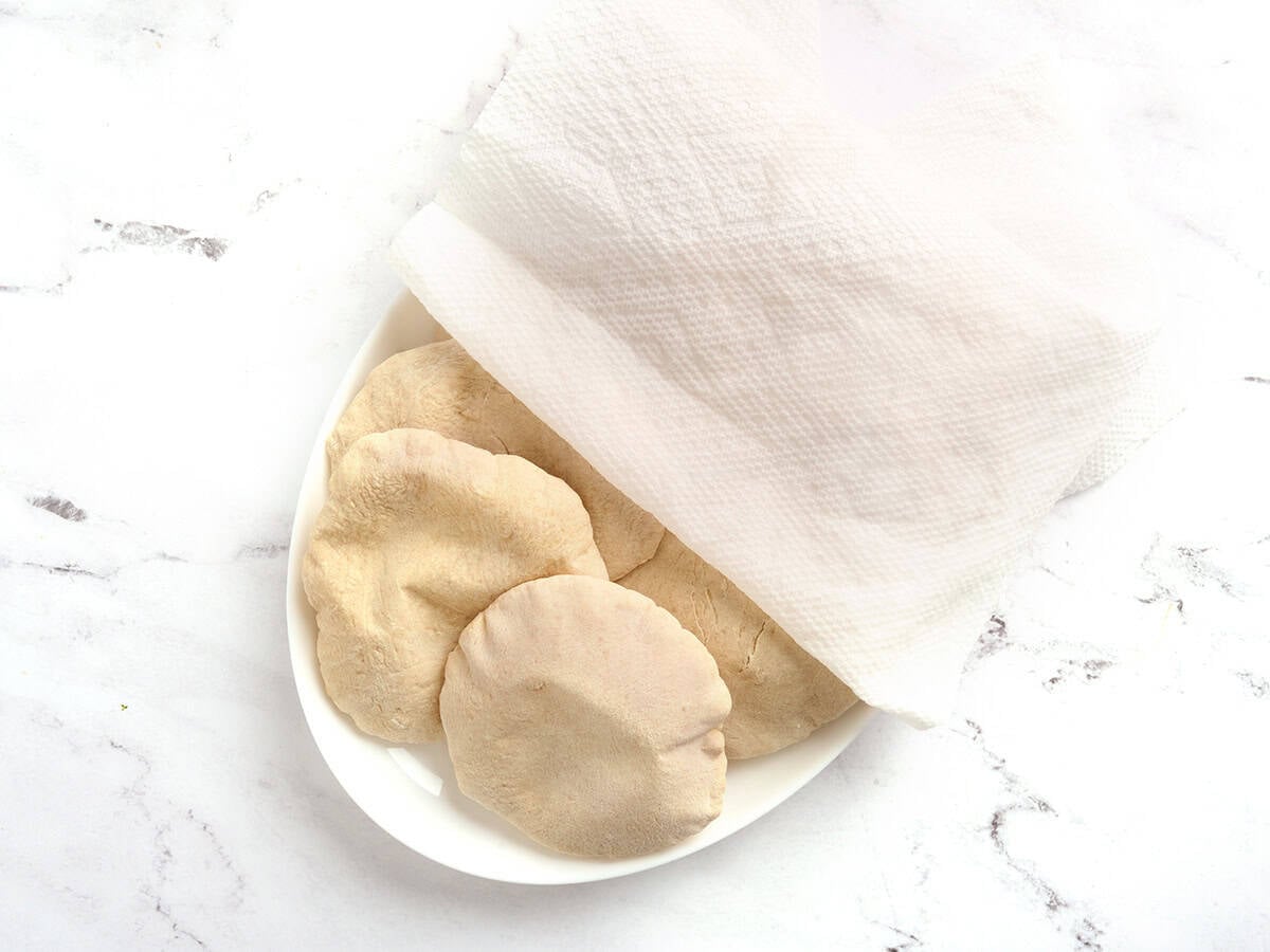 Homemade pita bread on a platter being covered with a damp cloth.