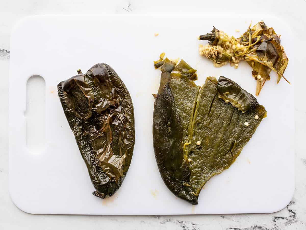 Peeled poblanos on a cutting board one with the seeds scraped out