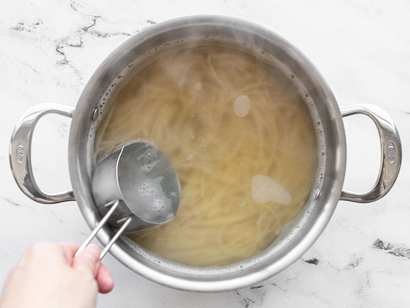 A measuring cup scooping out starchy pasta water from the pot