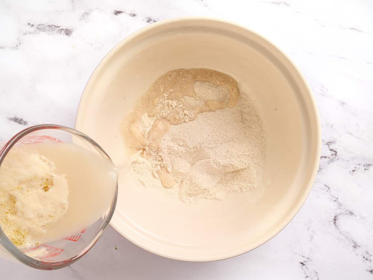 A yeast mixture being poured into a bowl with dry ingredients to make pita bread.