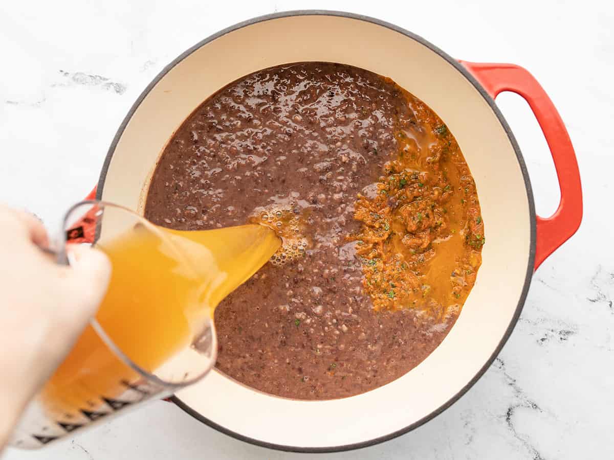 Vegetable broth being poured into the soup pot with vegetables and beans