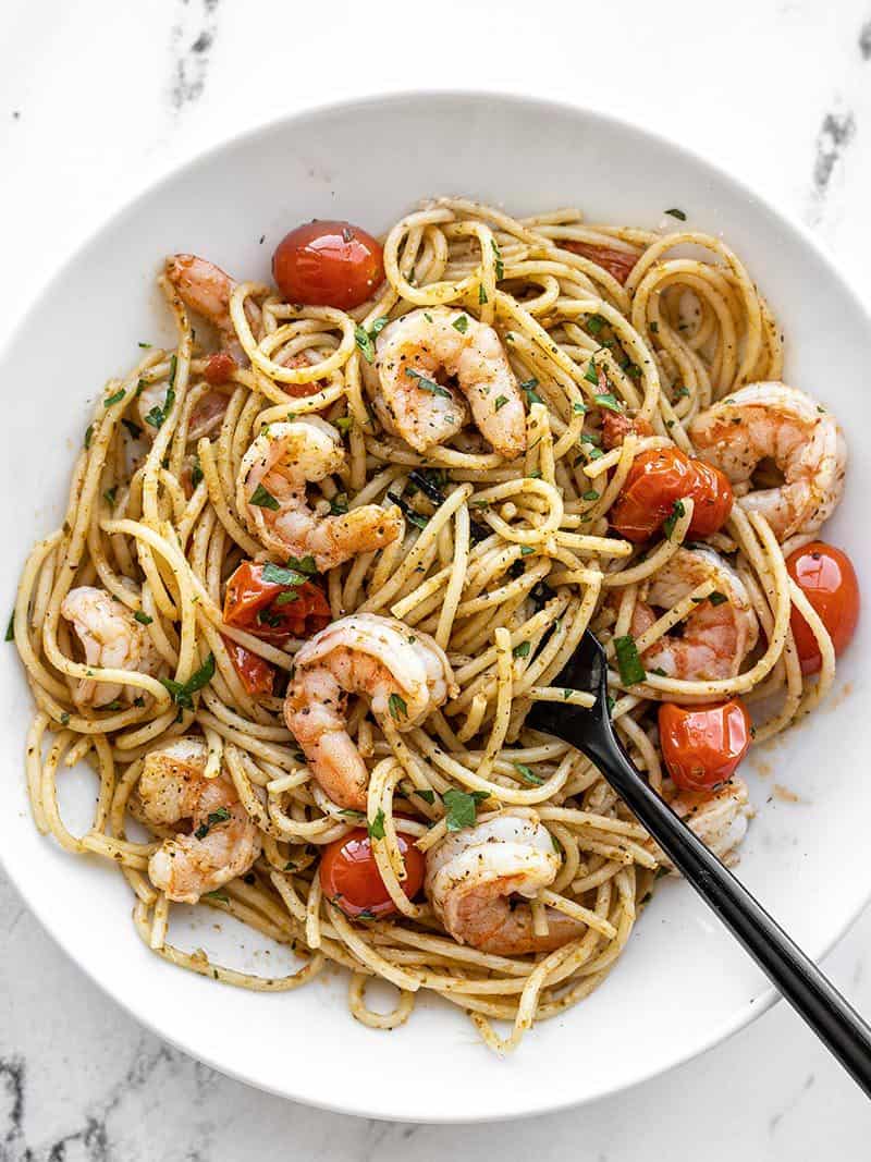 Overhead view of a bowl full of pesto shrimp pasta with a black fork in the middle