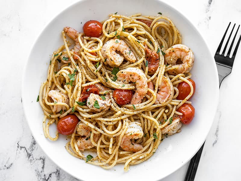 Overhead view of a finished bowl of pesto shrimp pasta with a fork on the side