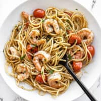 Overhead view of a bowl full of pesto shrimp pasta with a black fork in the center