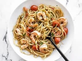 Overhead view of a bowl full of pesto shrimp pasta with a black fork in the center