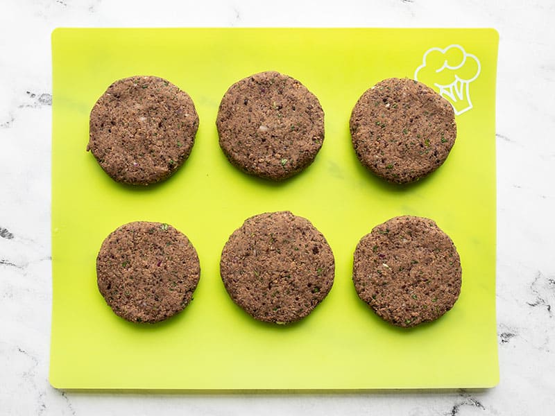 Shaped black bean burgers on a green cutting board