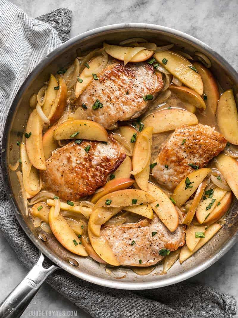 A skillet full of Apple Spice Pork Chops with parsley sprinkled over top