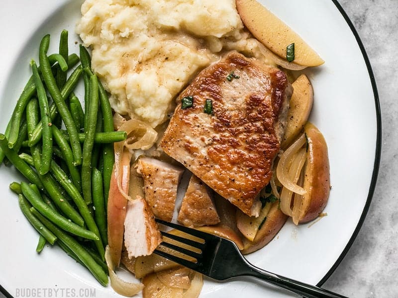 Sliced Apple Spice Pork Chops on a white plate with mashed potatoes and green beans.